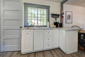 A kitchen with white cabinets, a window, a sink, and a coffee machine.