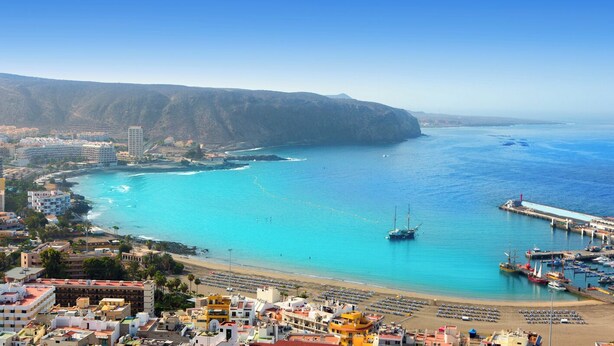 A coastal town with a beach, a pier, and a mountainous backdrop.