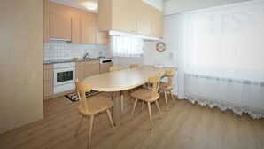Keittiössä on puukehikoiset kaapit, valkoinen liesi ja ruokapöytä tuoleineen.