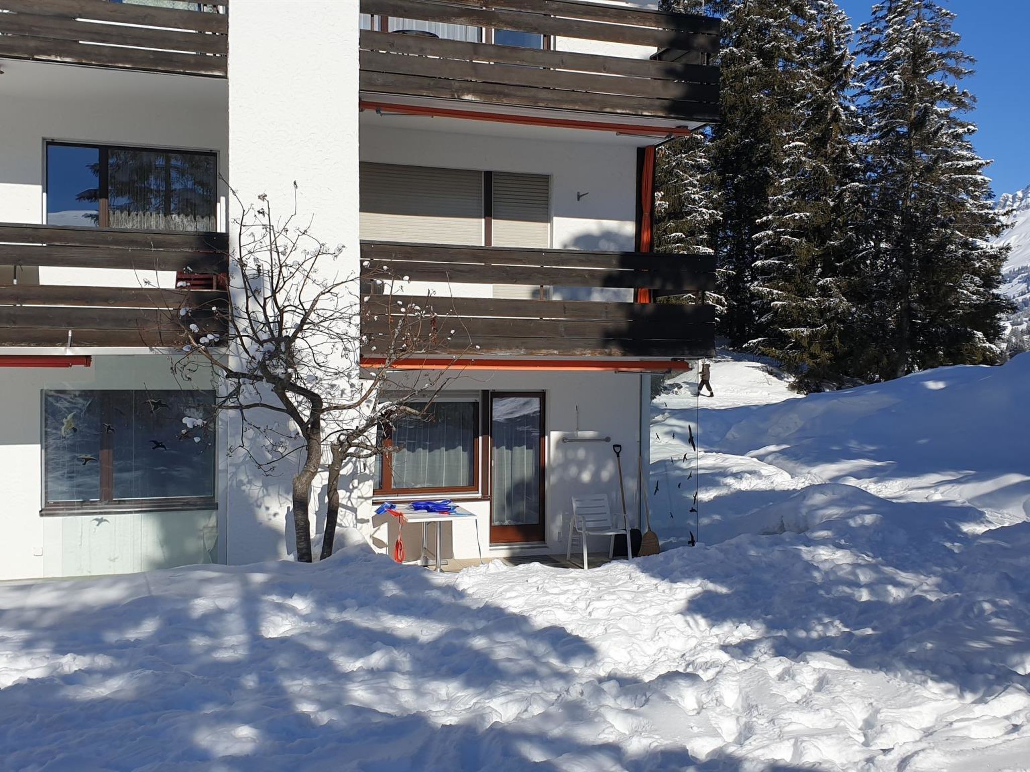 A modern building with multiple balconies, a snow-covered ground, and a tree in front.