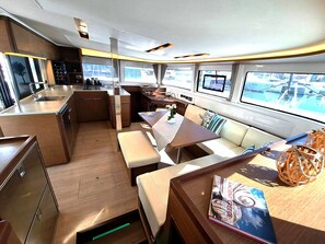 Une cuisine compacte dotée d’appareils électroménagers modernes, un coin repas avec un banc, et une vue sur la mer grâce à de grandes fenêtres.