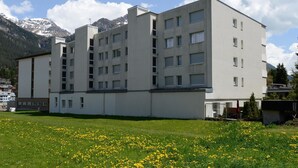 Un edificio de varios pisos con techo plano, amplios ventanales y un área verde con flores amarillas al frente.
