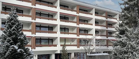 Een meerlaags gebouw met balkons, omringd door met sneeuw bedekte bomen.