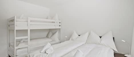 A bunk bed room with white bedding and pillows, a bedside table, and a lamp.