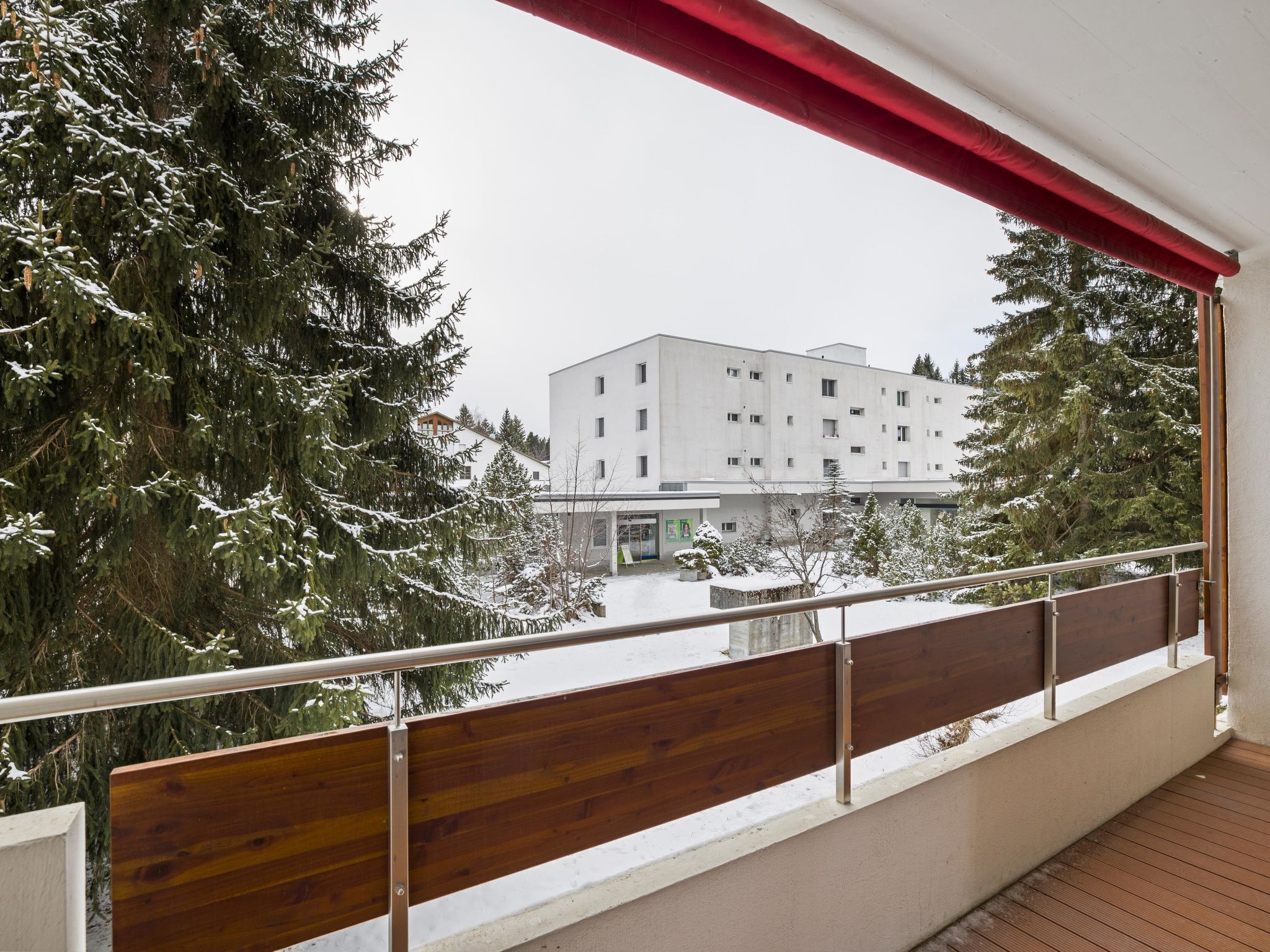 A balcony with a view of a building and snow-covered trees.