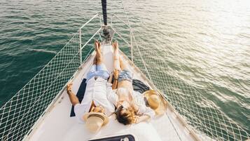 Two people lying on a boat deck with a netted railing, facing the water.