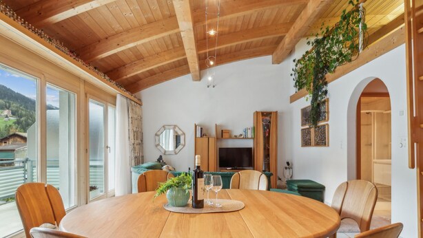 Un tavolo rotondo in legno con sedie, una bottiglia di vino e bicchieri su un tappetino.