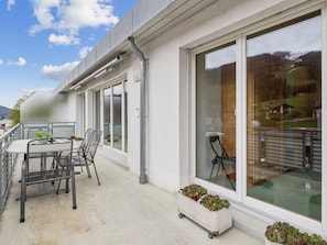 A balcony with a table and chairs, a potted plant, and a view of a snowy landscape through large windows. - Casa Hermi Appartement/Fewo 2.5 Zimmerwohnung by Interhome (Churwalden)