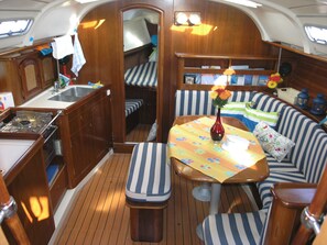 A compact galley with a sink, stove, and storage cabinets. There is a small table with a vase of flowers and a striped sofa with cushions. - Sun-Kissed Sailing Adventure in the Ionian Islands, Lefkada (Lefkada)