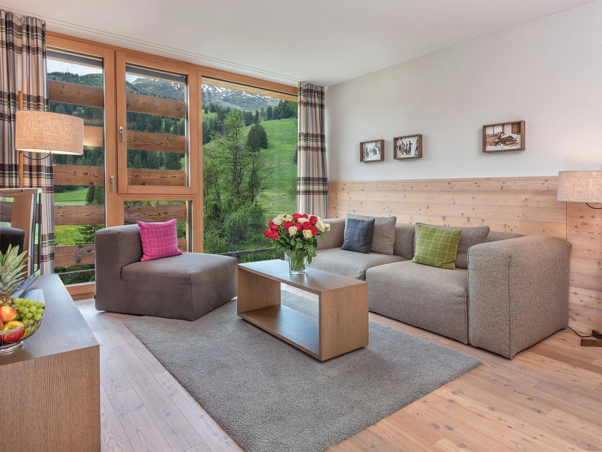 A modern living room with a sofa, armchair, and a coffee table. There are large windows with a view of a green landscape.