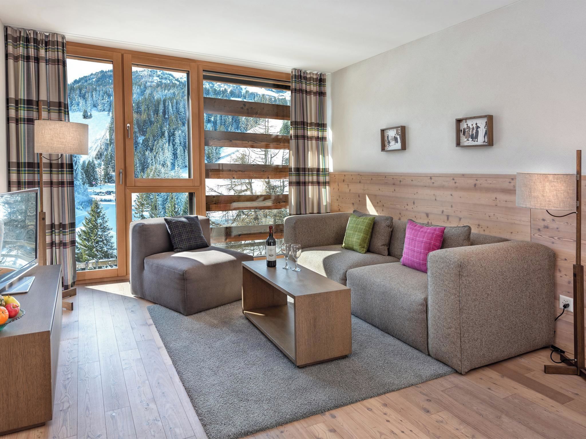 A modern living room with a sofa set, a coffee table, and a view of a snowy mountain landscape through large windows.