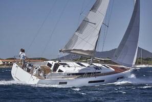 A sailboat with a cabin and deck area, sailing on water with a mountainous backdrop.