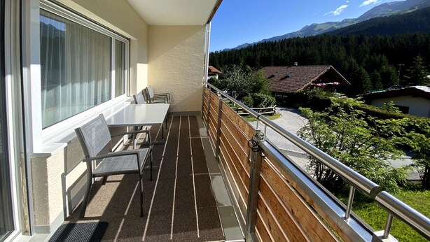A balcony with a table and chairs, a view of a mountain range, and a wooden railing. - Haus Montana 1/1 Appartement/Fewo,   6-Bettwohnung by Interhome (Lenzerheide)