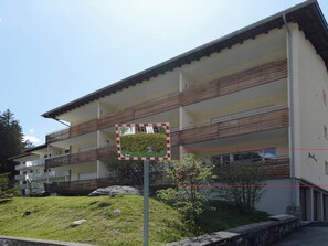 Ein mehrstöckiges Gebäude mit Balkonen, einer Rasenfläche und einem Schild mit Spiegelung.