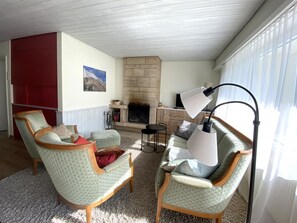 Ein Wohnzimmer mit Kamin, zwei Sesseln, einer Couch und einem Tisch.