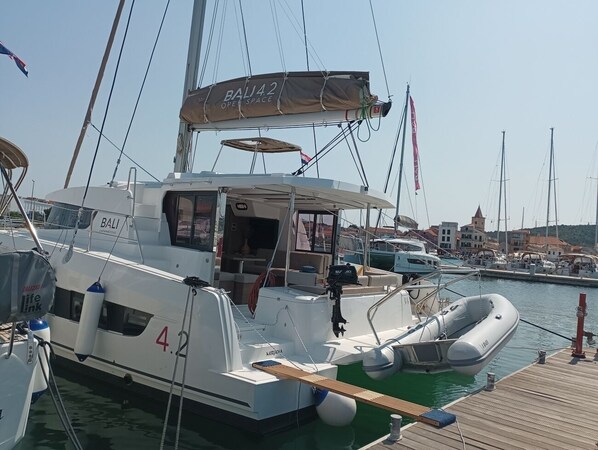 Uma marina com barcos atracados, incluindo um barco branco com 'BALJI' e '4.2' visíveis, e um pequeno bote inflável.