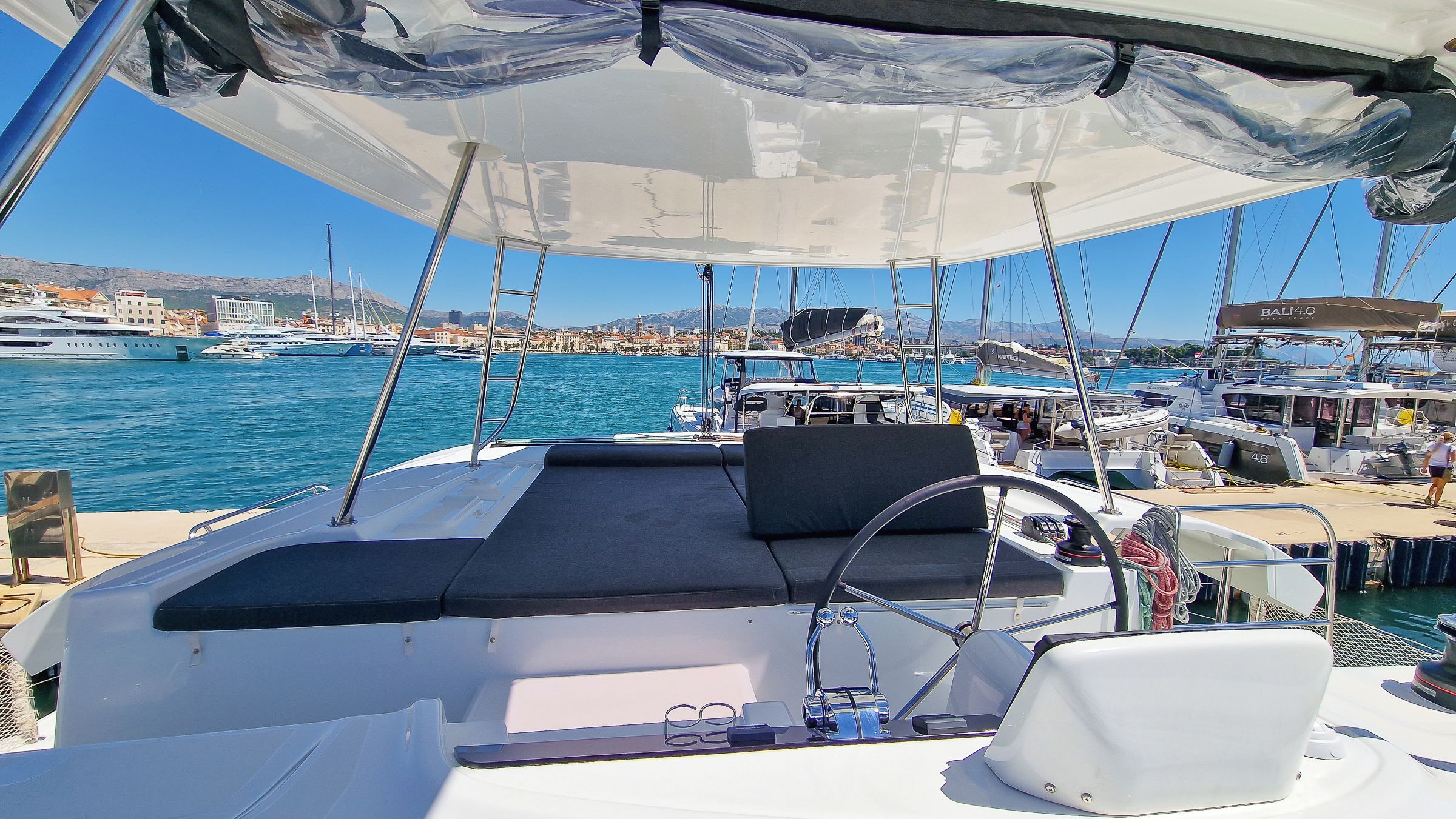 A boat's deck with a steering wheel, a cushioned seating area, and a clear view of the marina and cityscape in the background.
