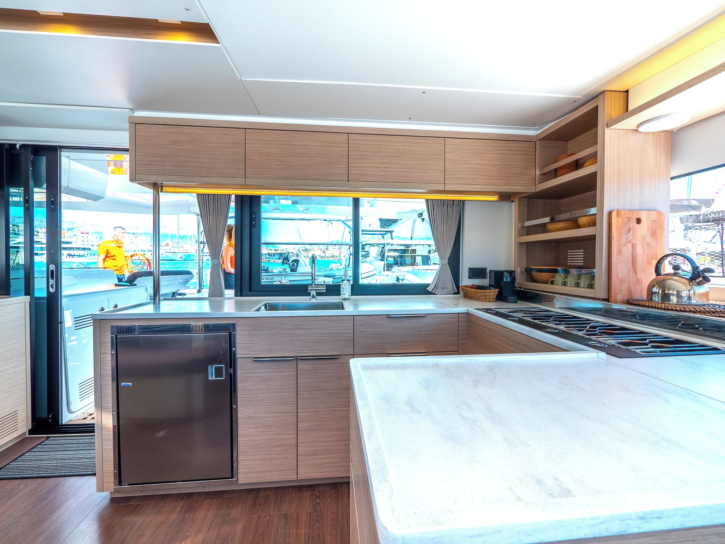 Une cuisine moderne dotée d’un lave-vaisselle intégré, d’un grand îlot central et offrant une vue sur le port de plaisance.