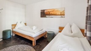 Een hotelkamer met een bed, nachtkastje, stoel, schilderij aan de muur en gordijn.