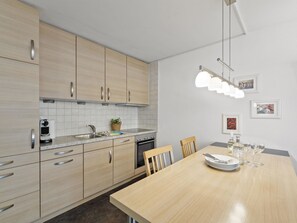 A modern kitchen with light wood cabinets, a granite countertop, a built-in oven, and a dining area with a wooden table set for four. - Nr.08 Haus Sursilvana Appartement/Fewo,   Nr.08 Haus Sursilvana by Interhome (Lenzerheide)