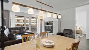 Een moderne woonkamer met een eethoek, met een bank, een eettafel gedekt met borden, glazen en een fles, en hanglampen erboven.