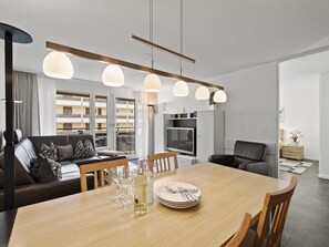 A modern living room with a dining area, featuring a sofa, a dining table set with plates, glasses, and a bottle, and pendant lights above. - Nr.08 Haus Sursilvana Appartement/Fewo,   Nr.08 Haus Sursilvana by Interhome (Lenzerheide)
