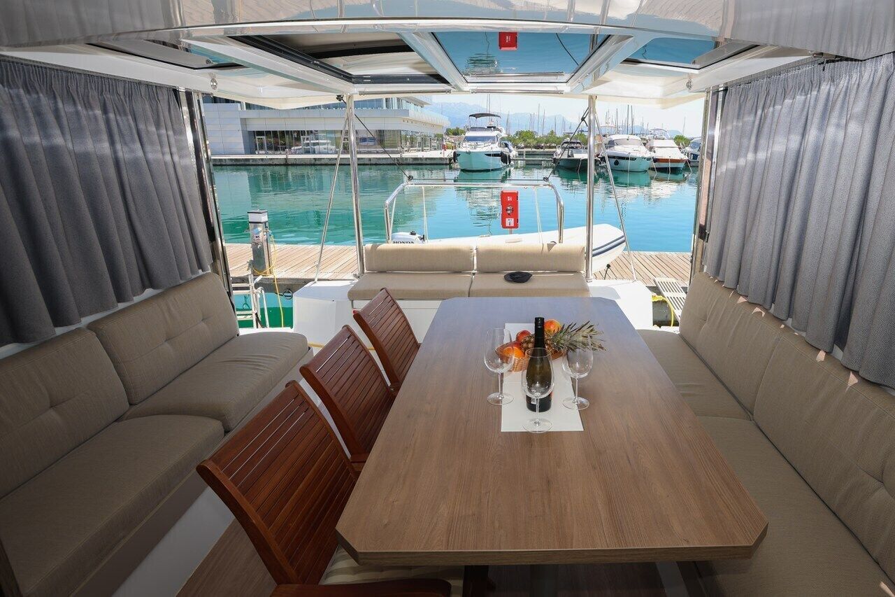 Interni di uno yacht con zona pranzo, sedute imbottite e vista sul porto turistico.