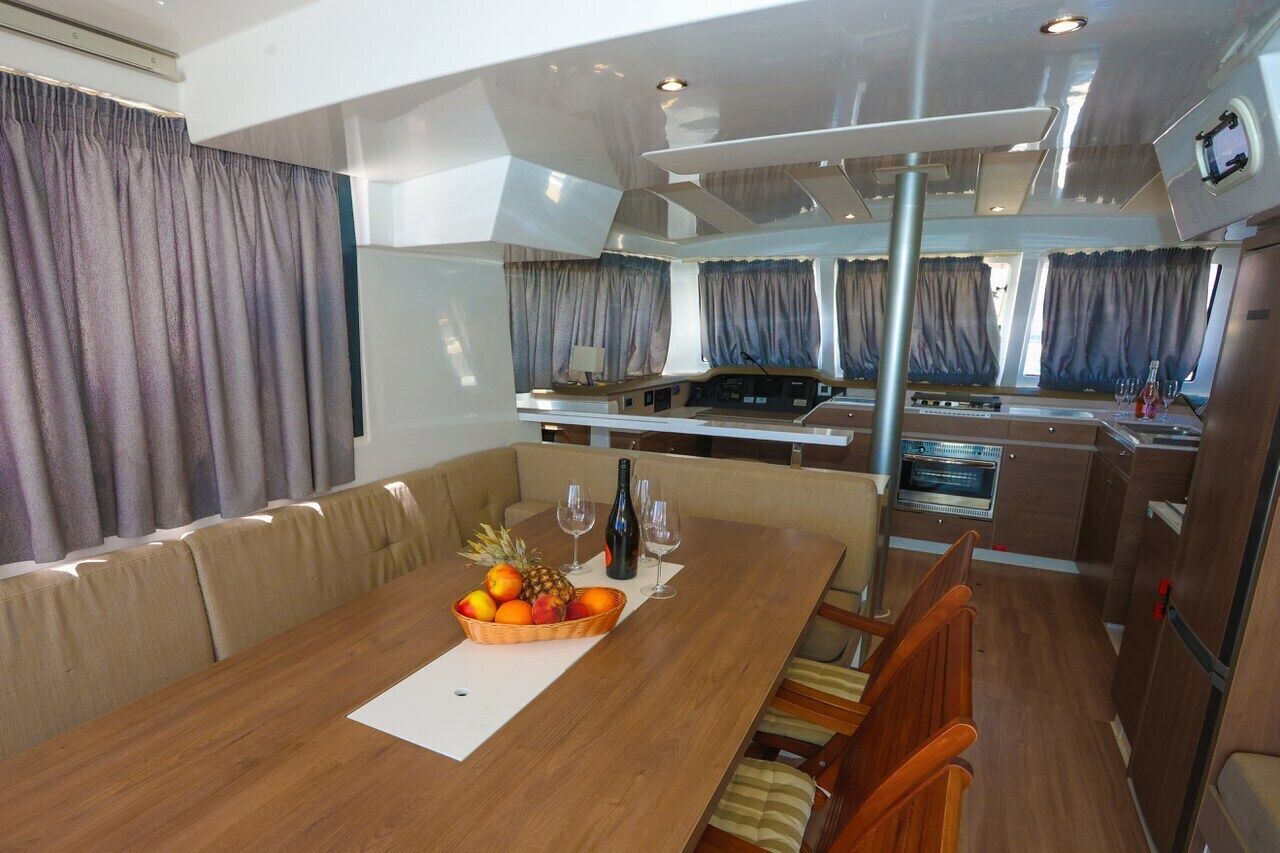 A compact kitchen with a dining area, a central table with fruit and wine glasses, and a view of the kitchen through a window.