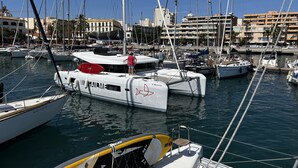 A marina with multiple boats docked, a clear sky, and buildings in the background. - Sun-Kissed Sailing Adventure in the Majestic Islas Baleares (Ibiza / Eivissa)