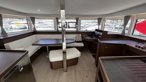 A boat interior with a dining area, a small kitchen, and a seating area with a view of the marina. - Sun-Kissed Sailing Adventure in the Majestic Islas Baleares (Ibiza / Eivissa)