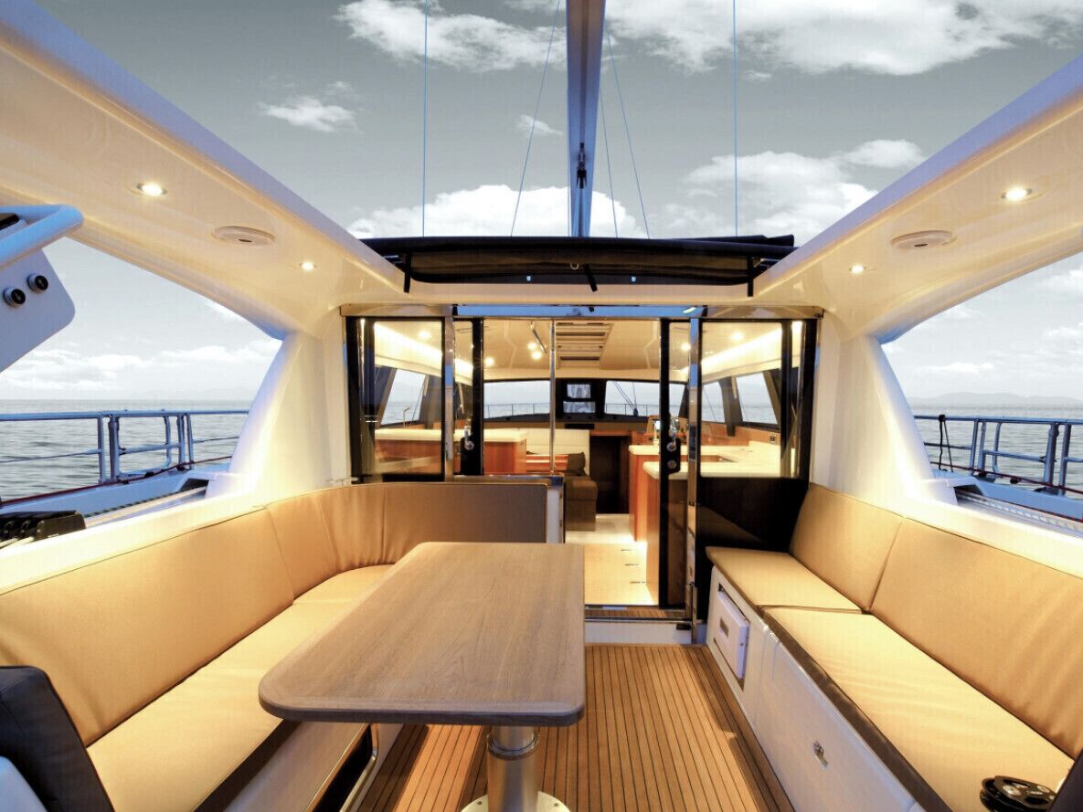 A boat interior with a central table, cushioned seating, and a view of the sea.