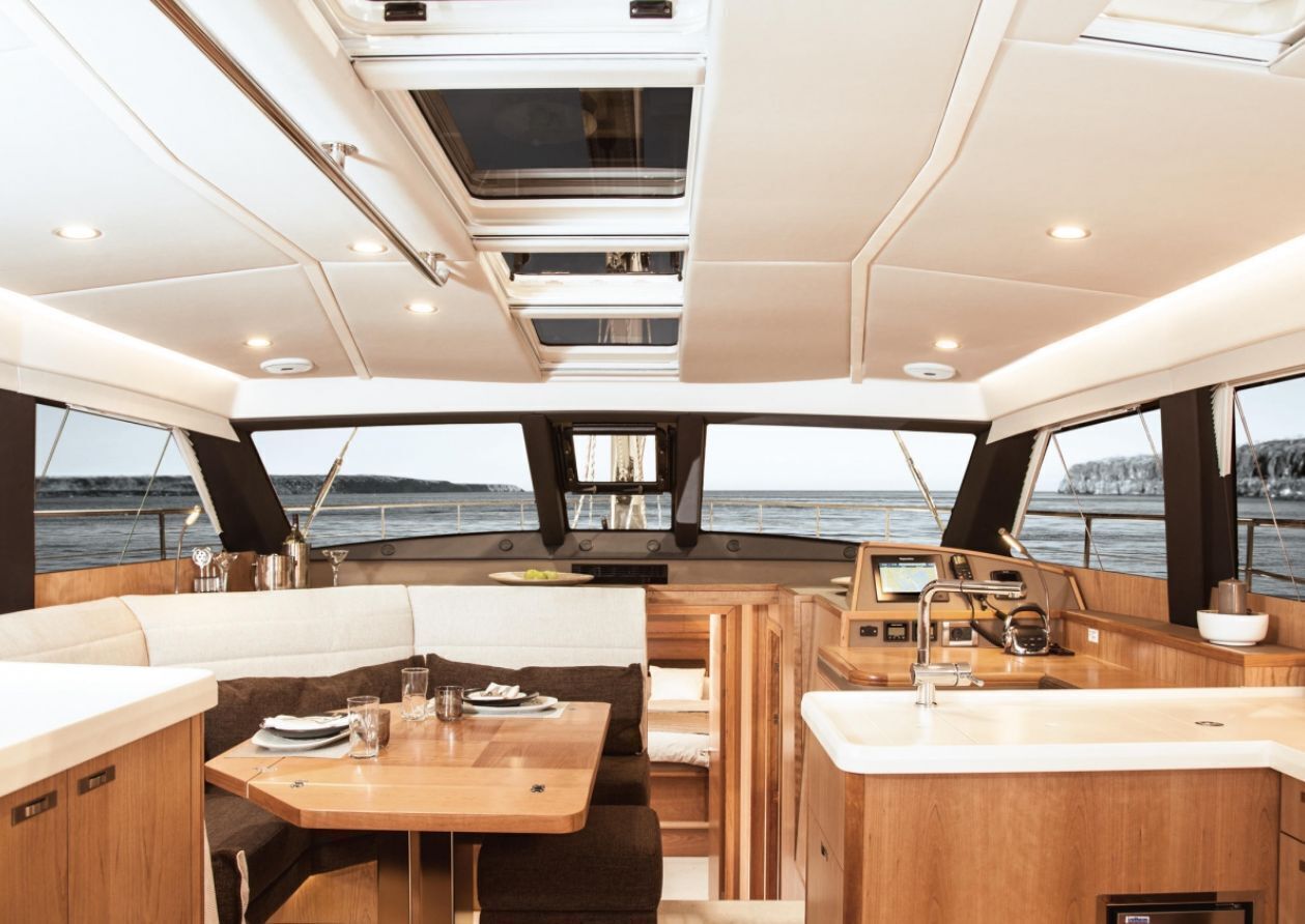 Interieur van een jacht met een eethoek, zitgedeelte, keuken en uitzicht op zee.