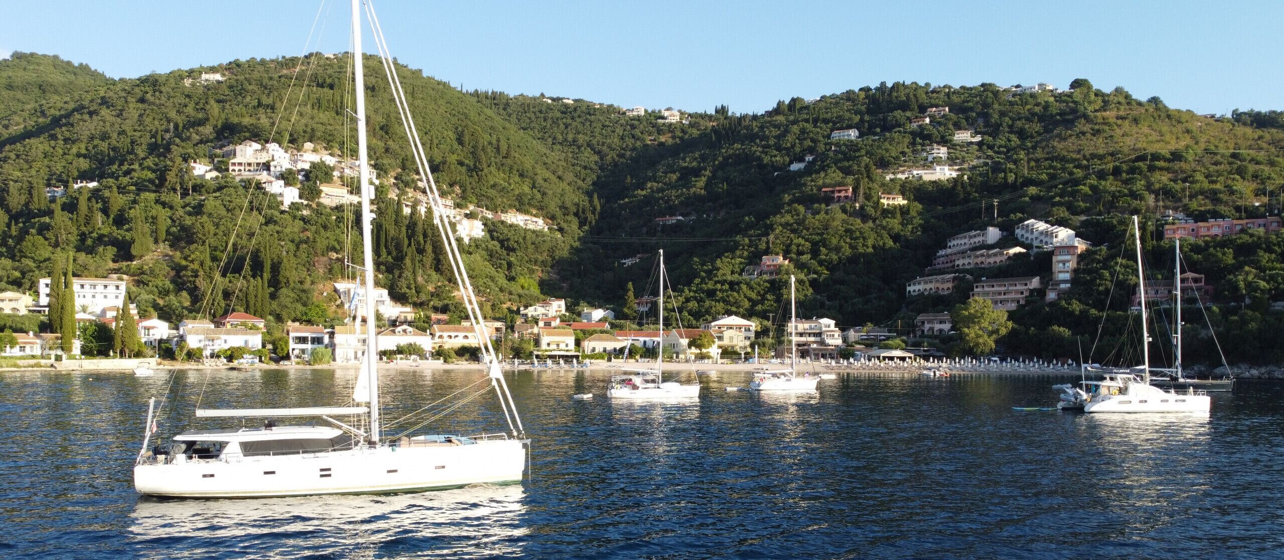 Un port de plaisance avec des voiliers, une colline parsemée de bâtiments et un ciel dégagé.