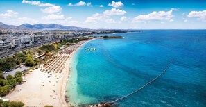Un paysage urbain côtier avec une plage, une eau d’un bleu limpide et une chaîne de montagnes à l’horizon.