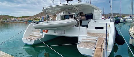 Un yacht blanc était amarré dans une marina, avec une terrasse couverte, une cabine visible et une petite rampe d’accès pour les bateaux.