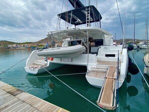 Un yacht blanc était amarré dans une marina, avec une terrasse couverte, une cabine visible et une petite rampe d’accès pour les bateaux.