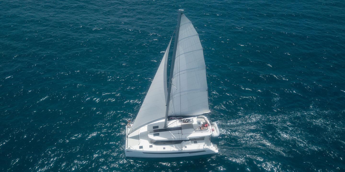 Un velero con casco blanco y una vela grande, flotando sobre el agua.