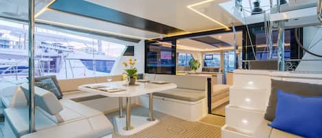 A modern yacht interior with a dining area, seating, and a view of the marina.