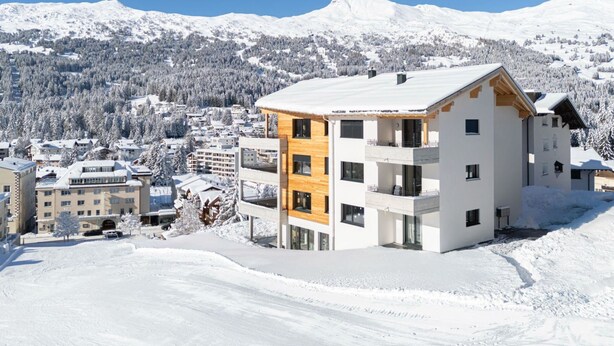 Un hotel moderno de varios pisos con techo plano, situado en una zona montañosa nevada.