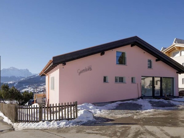 A pink building with a sign reading 'Guardia Val' and a wooden fence in front.