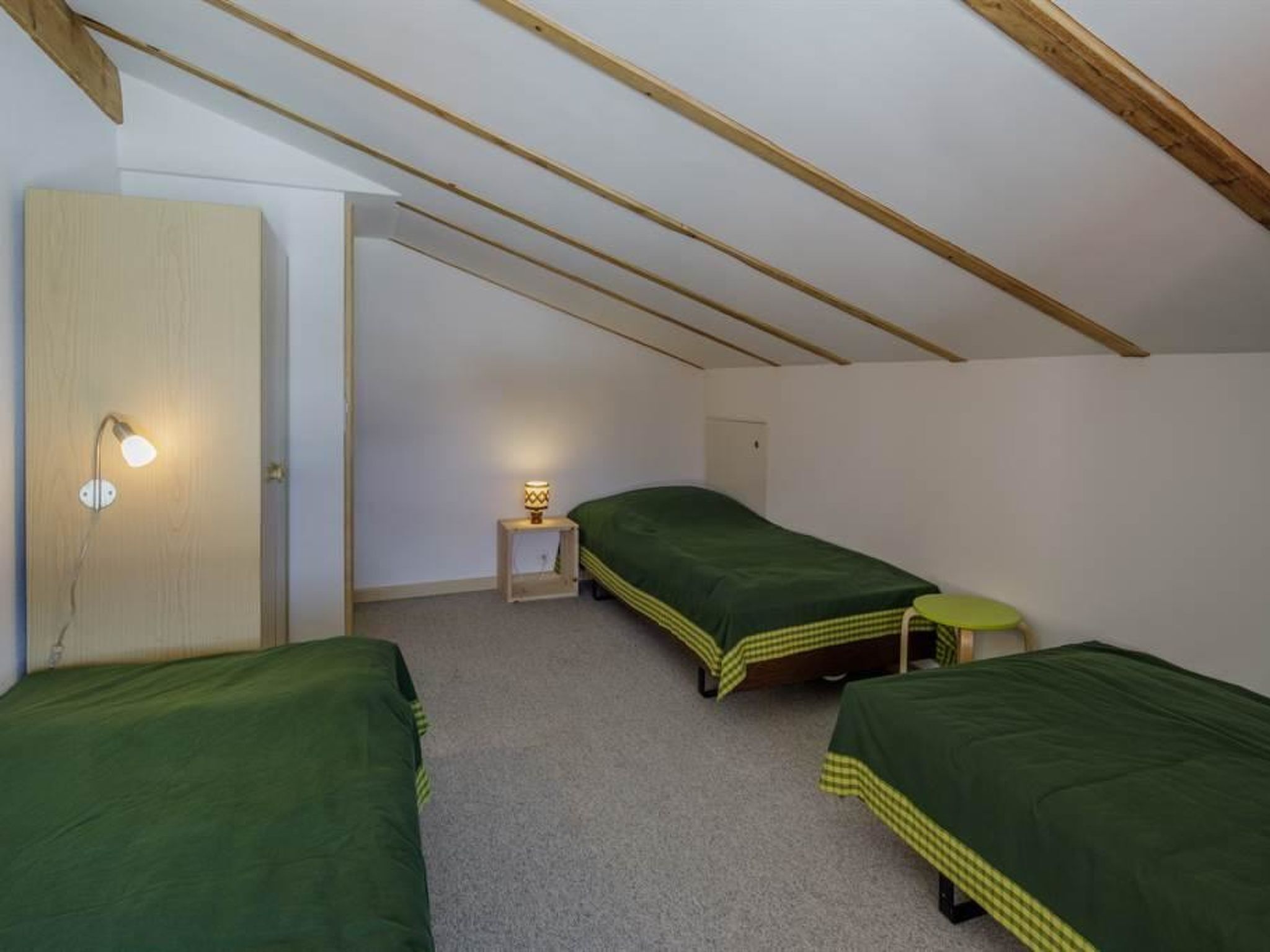 Eine kleine Einzelunterkunft mit zwei Betten, einem Nachttisch und einer an der Wand befestigten Lampe.