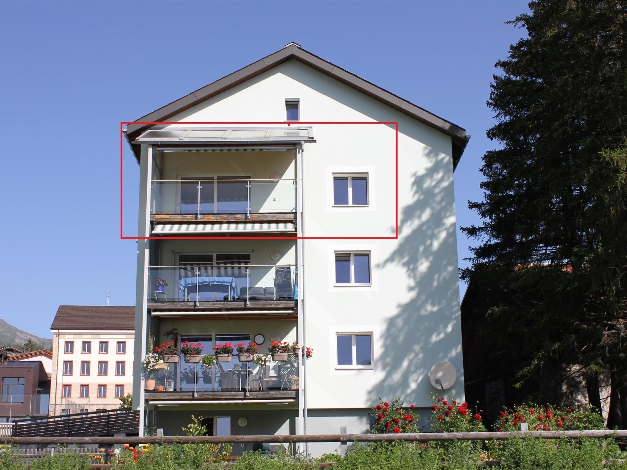 Ein mehrstöckiges Wohngebäude mit Balkonen, einer Satellitensch üssel und einem Garten mit roten Blüten.