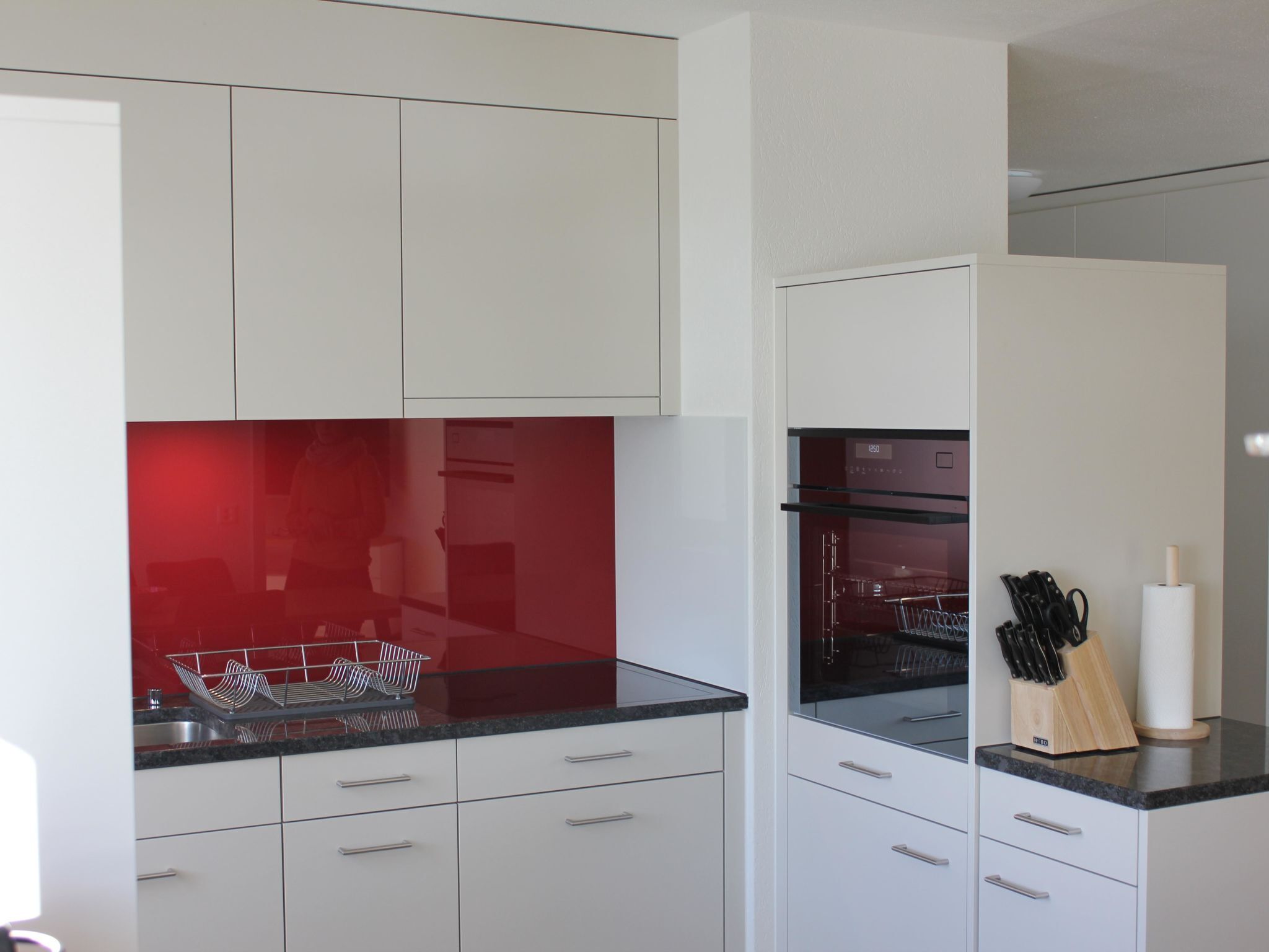 Una cucina moderna con mobili bianchi, uno schienale rosso e un forno incassato.