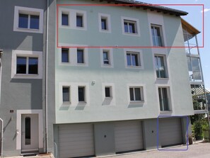 Ein mehrstöckiges Gebäude mit heller Fassade, zahlreichen Fenstern und einem Garagenzugang.