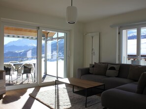 Ein modernes Wohnzimmer mit Sofa, Couchtisch und Blick auf Berge durch große Fenster.
