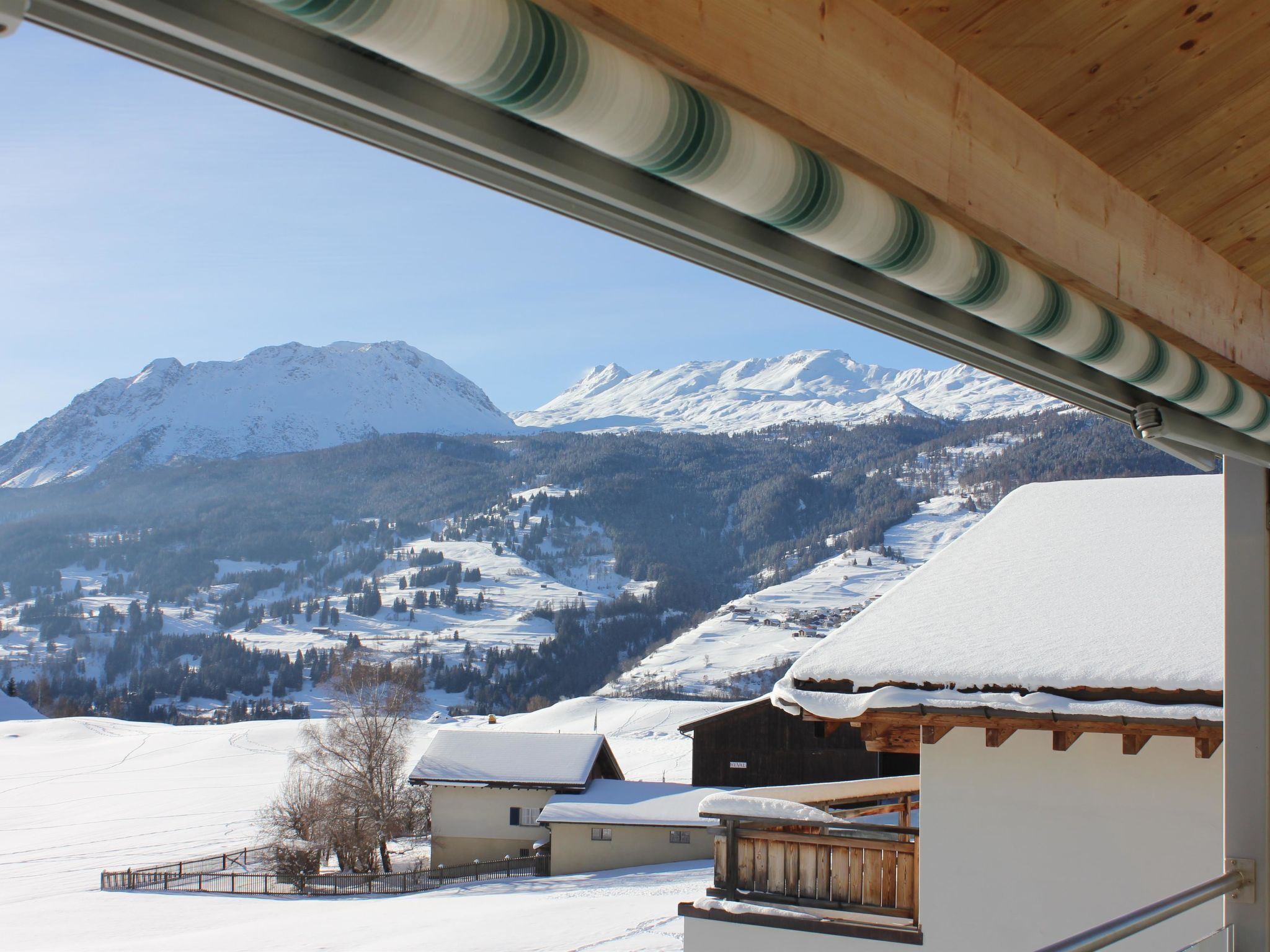 Eine verschneite Berglandschaft mit blauem Himmel, ein Holzkonstruktion mit Schnee bedecktem Dach und eine Metallstruktur im Vordergrund.