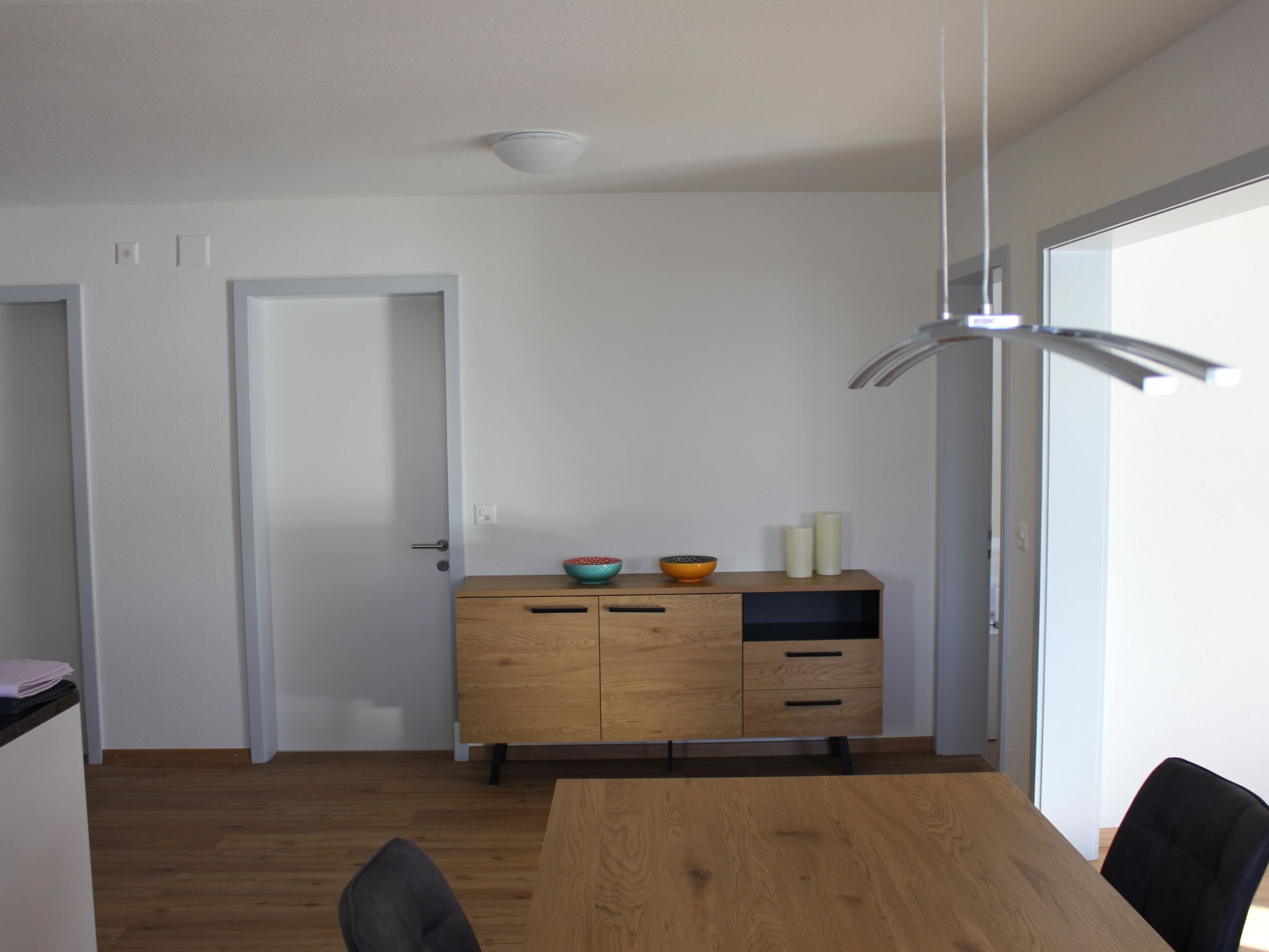 Ein Essbereich mit Holztisch, Stühlen, einem Schrank mit dekorativen Schalen und einer hängenden Leuchte.