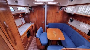 A compact interior with a wooden deck, a central table, and blue cushioned seating. - Sun-Kissed Sailing Adventure in Phuket (Mai Khao)