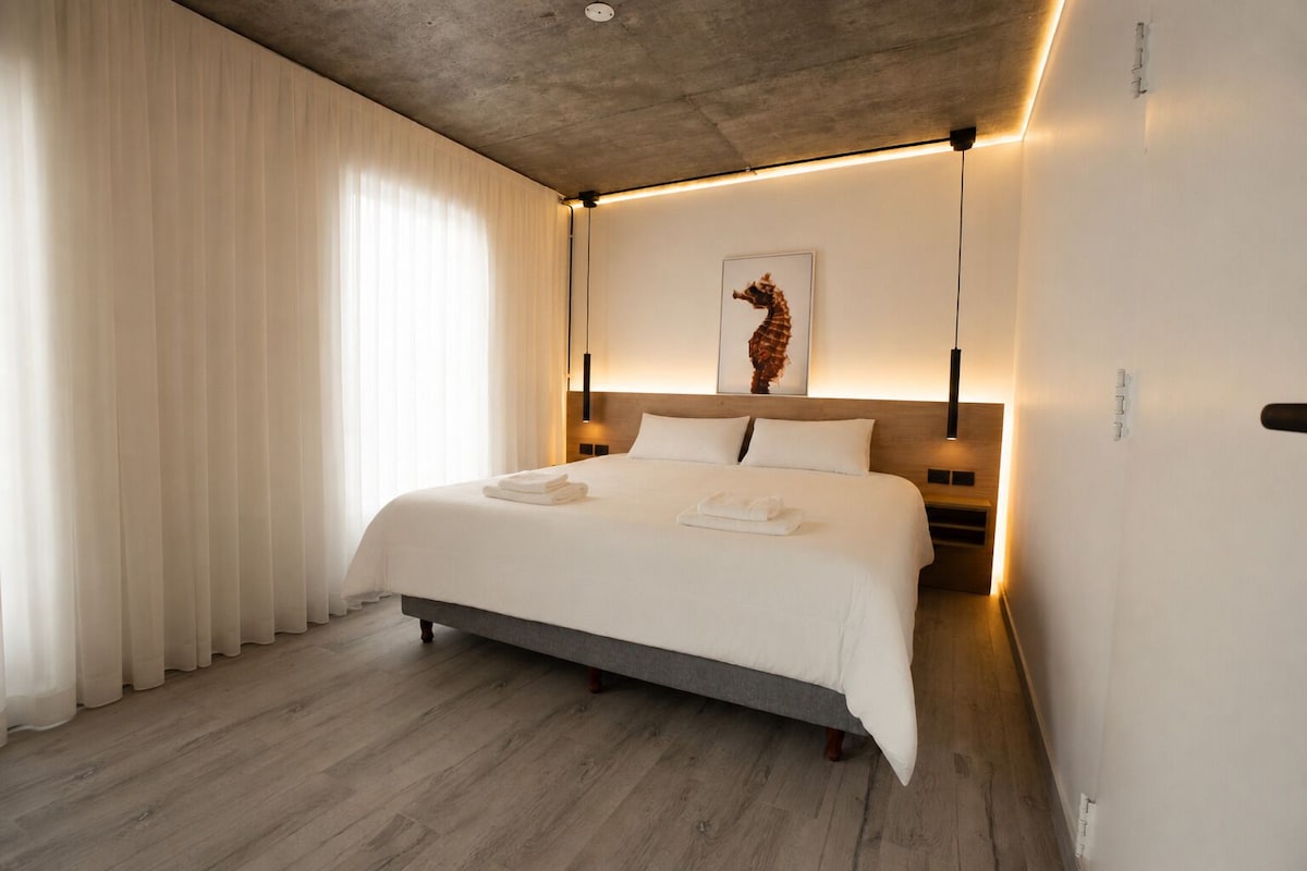 Una habitación de hotel moderna con una cama grande, suelo de madera y una obra de arte colgada en la pared.