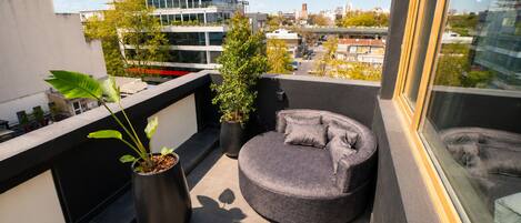 A rooftop terrace with a round seating area, potted plants, and a view of the cityscape.